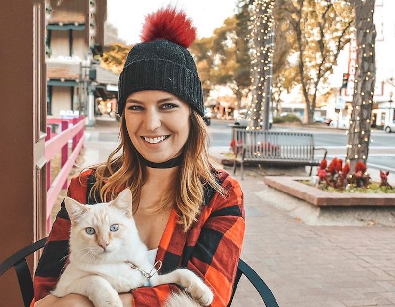 blonde girl with beanie holding her white cat outside during christmas in california