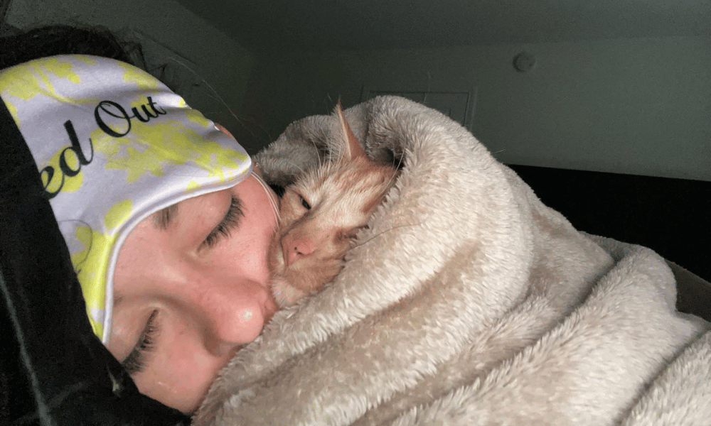 blonde girl cuddling in a blanker with her ginger cat